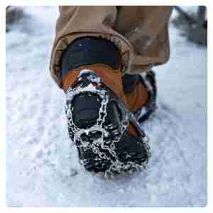 Mans feet in view showing ice cleats being worn on his boots for extra traction in the snow.